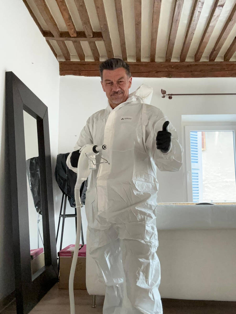 Technicien ACS38 en combinaison intégrale blanche dans une chambre, prêt à traiter un logement contre les punaises de lit